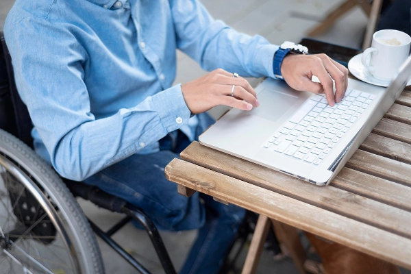man on wheelchair using laptop on bench